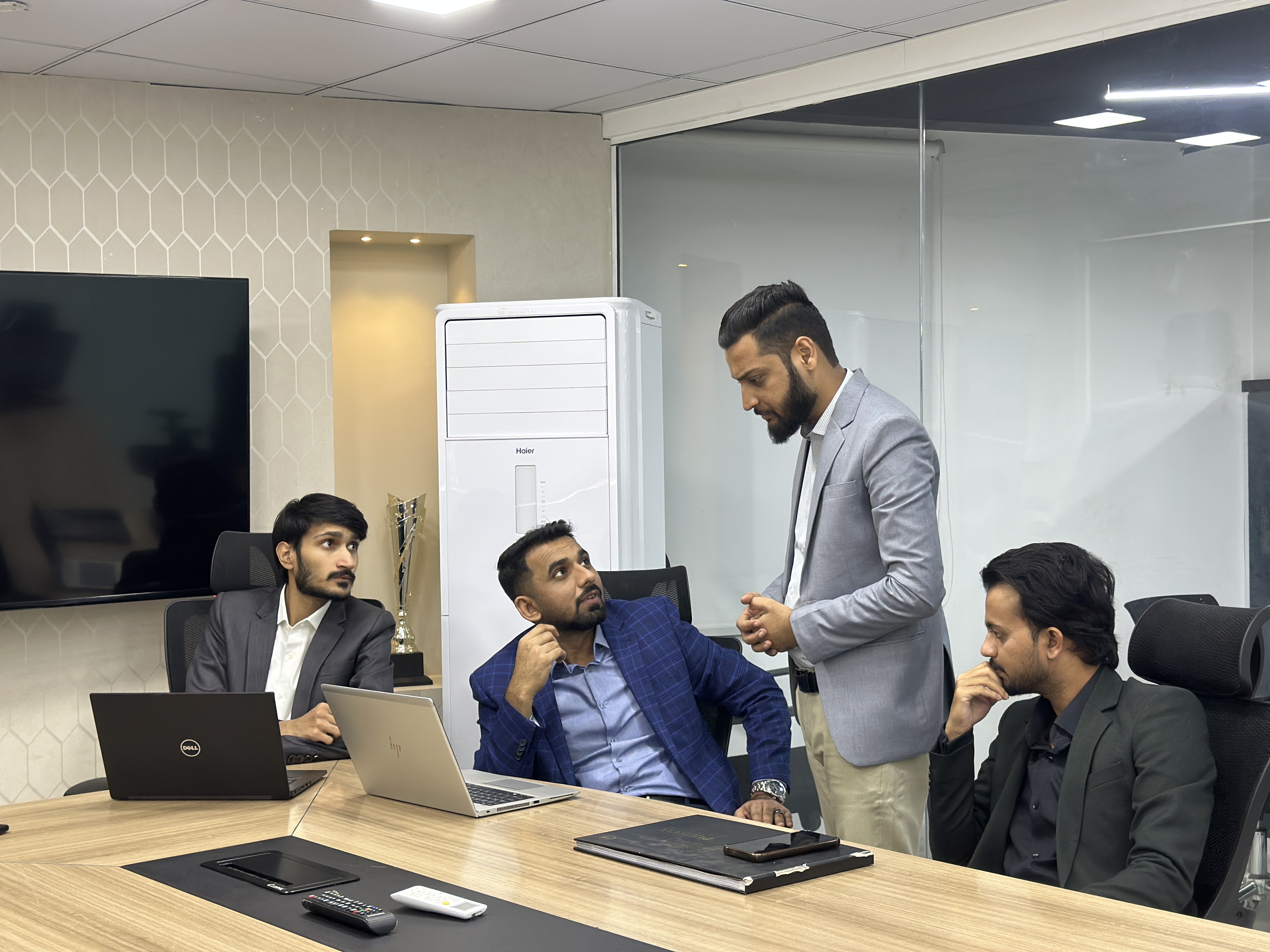 Five men in an office conference room, one leading a discussion at a modern wooden conference table